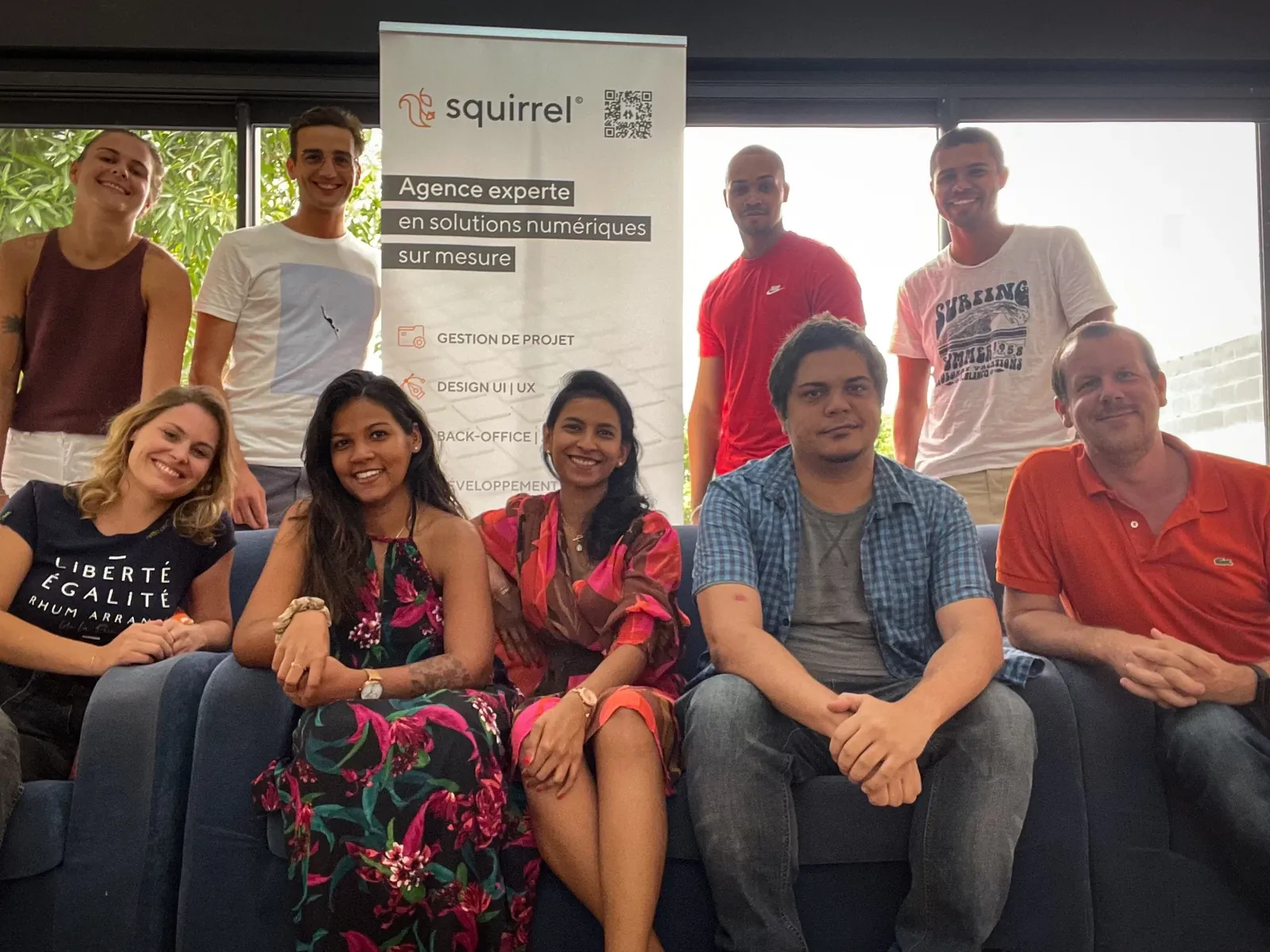 Dix membres de l'équipe Squirrel réunis dans une salle, devant le kakémono de l'agence « Agence experte en solutions numériques sur mesure »